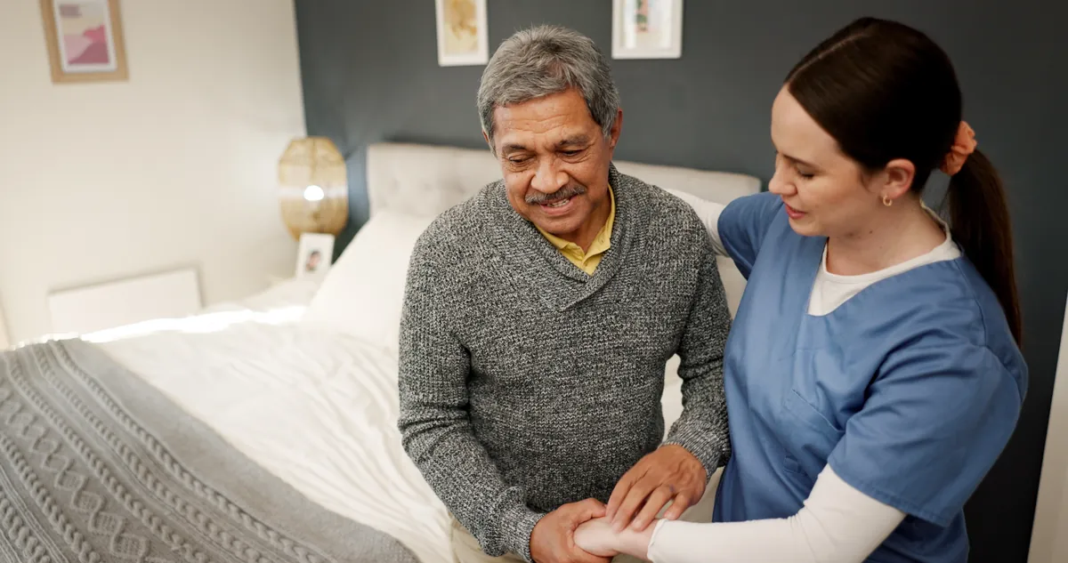 Support worker in blue scrubs helping an older man at home