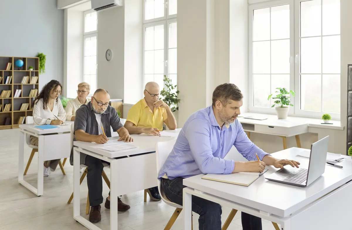 Adult learners of different ages working at desks in a bright classroom