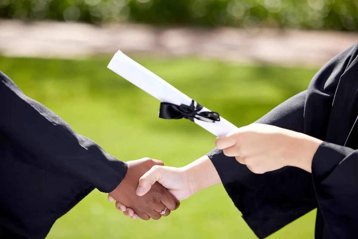 Rolled certificate handed over with a handshake against a green lawn
