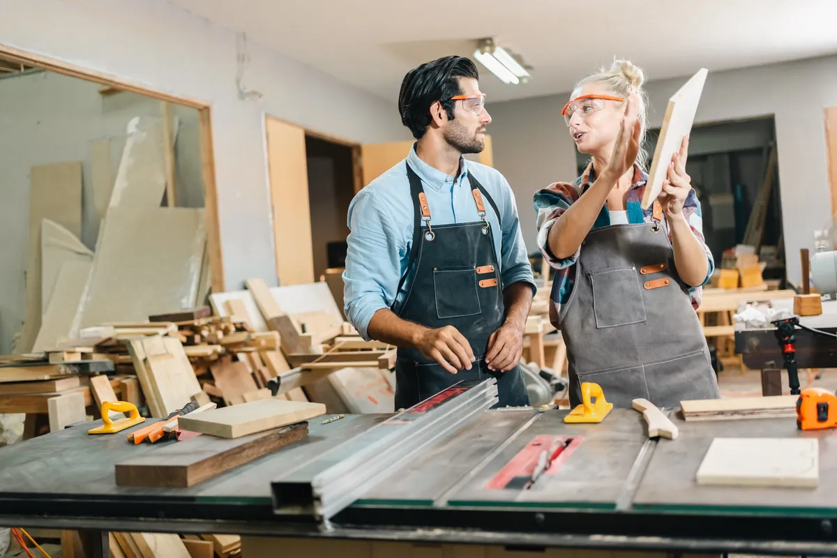 Two carpenters in aprons working together in a bright joinery workshop