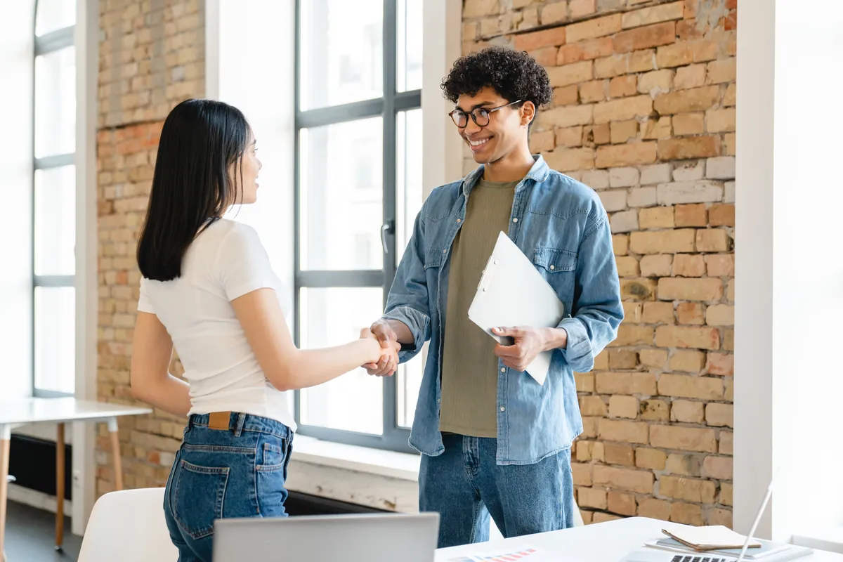 Young new starter shaking hands with a colleague in a bright office
