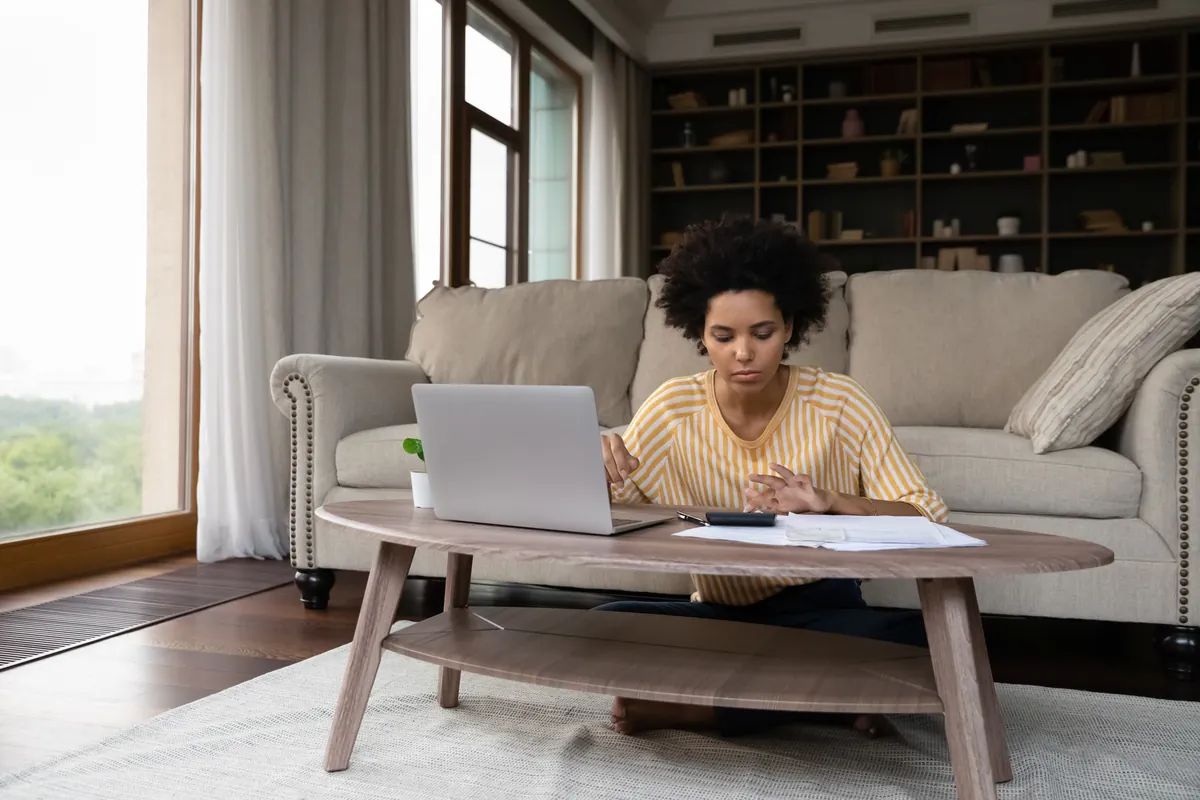 Woman working on a laptop with papers in a bright living room