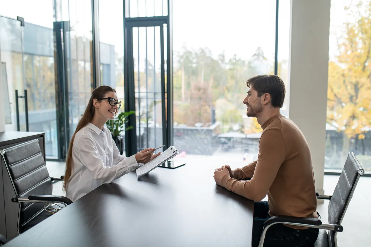 Job interview across a table in a bright modern glass-walled office