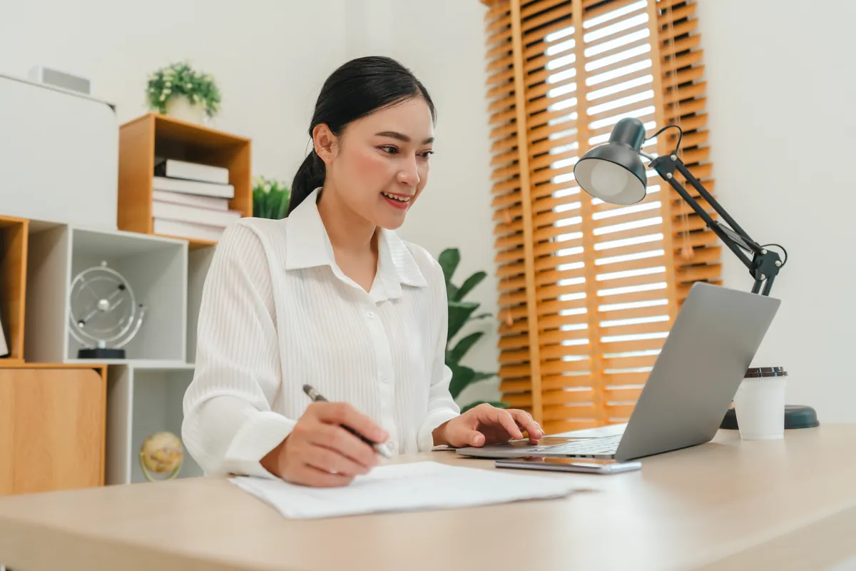 Woman preparing documents on a laptop at a bright desk